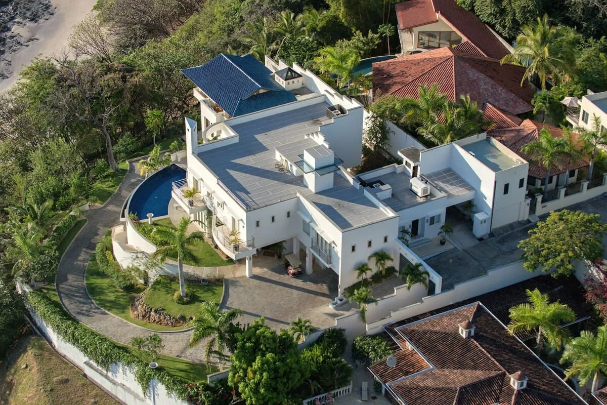 An aerial view of a large white building surrounded by greenery and nearby homes.