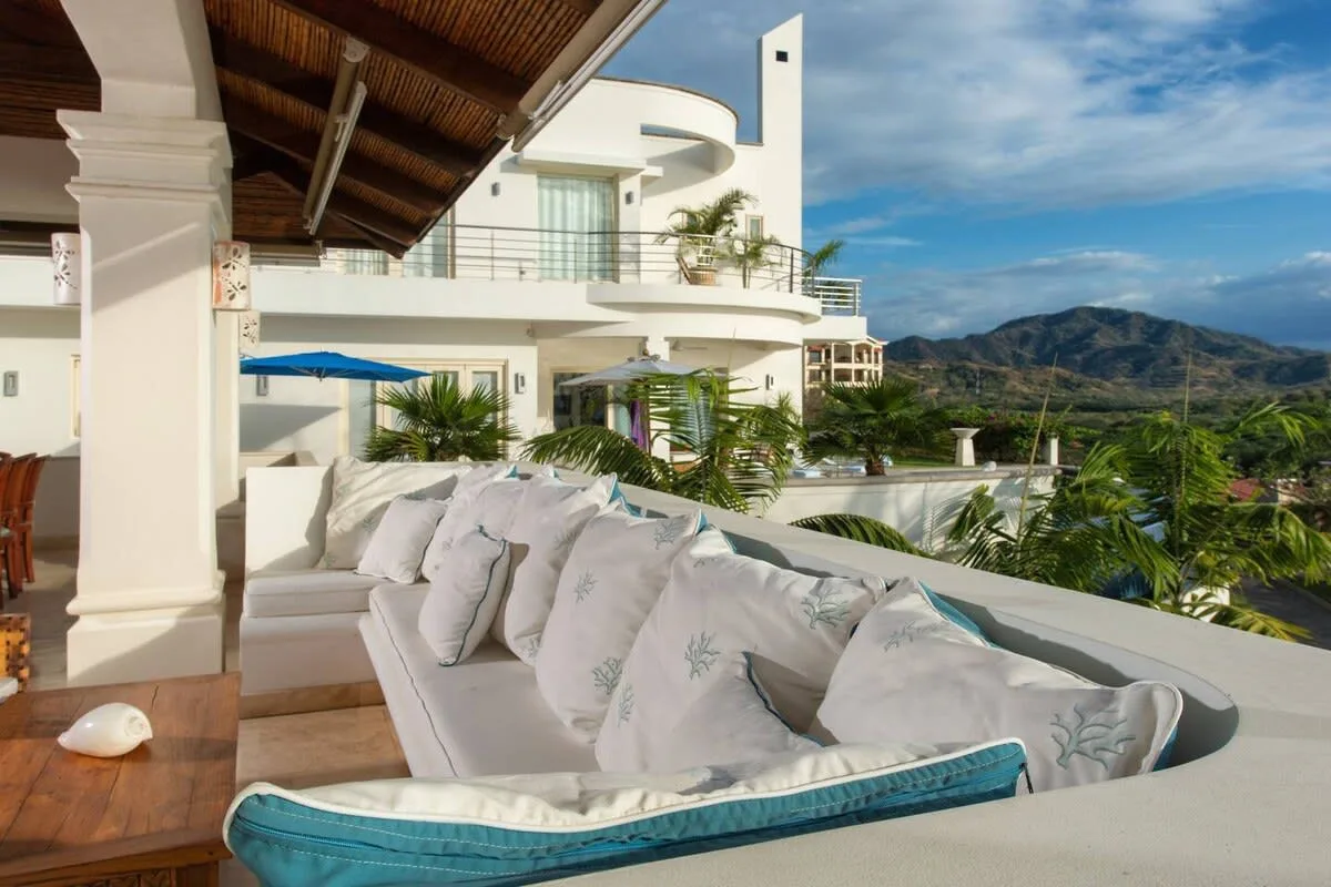 A covered outdoor lounge overlooks tropical greenery and distant mountains.