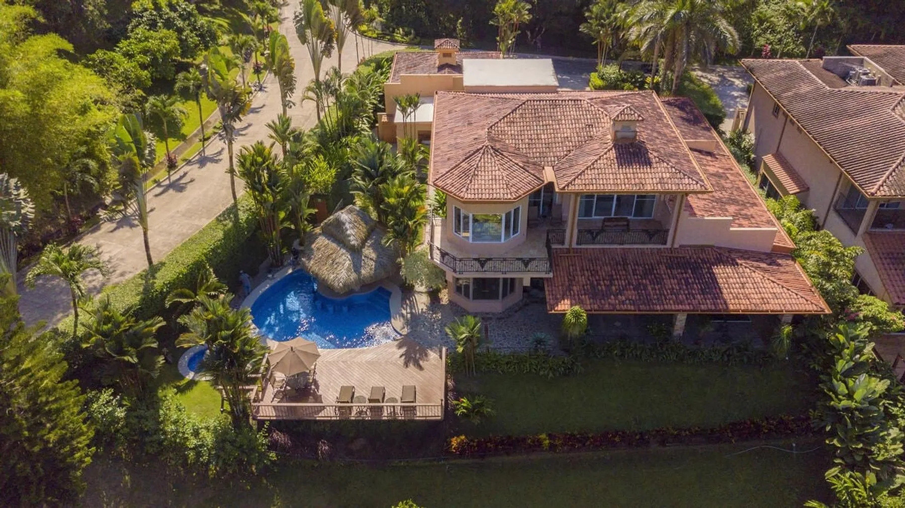 Una vista aérea muestra una casa junto a una piscina, rodeada de árboles y jardines.