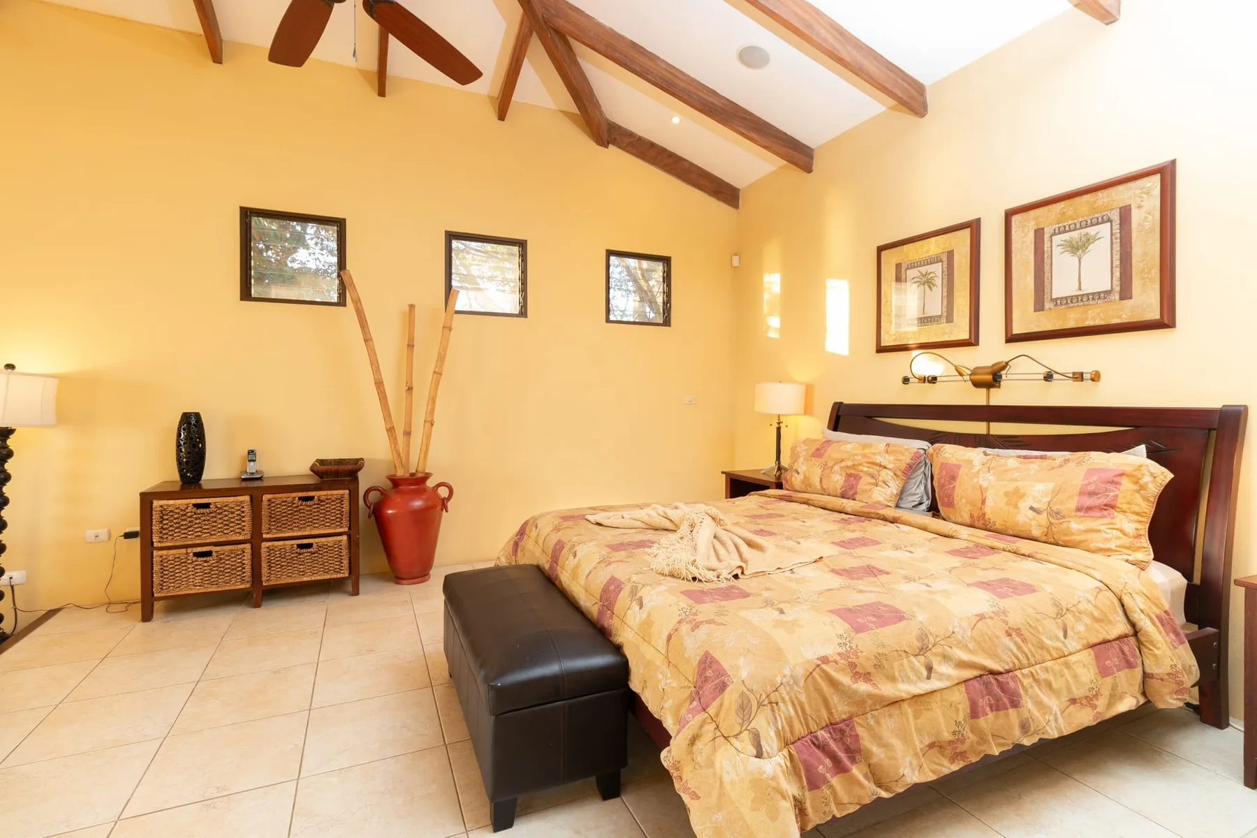 A bedroom with a large bed, a bench, and exposed wooden ceiling beams.