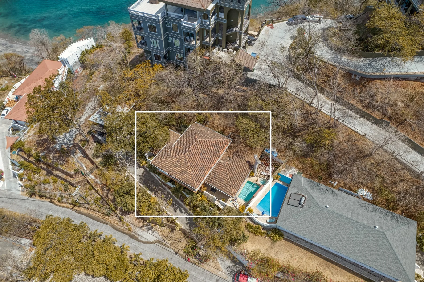 Aerial view of a tiled-roof building among trees, with a pool beside it.