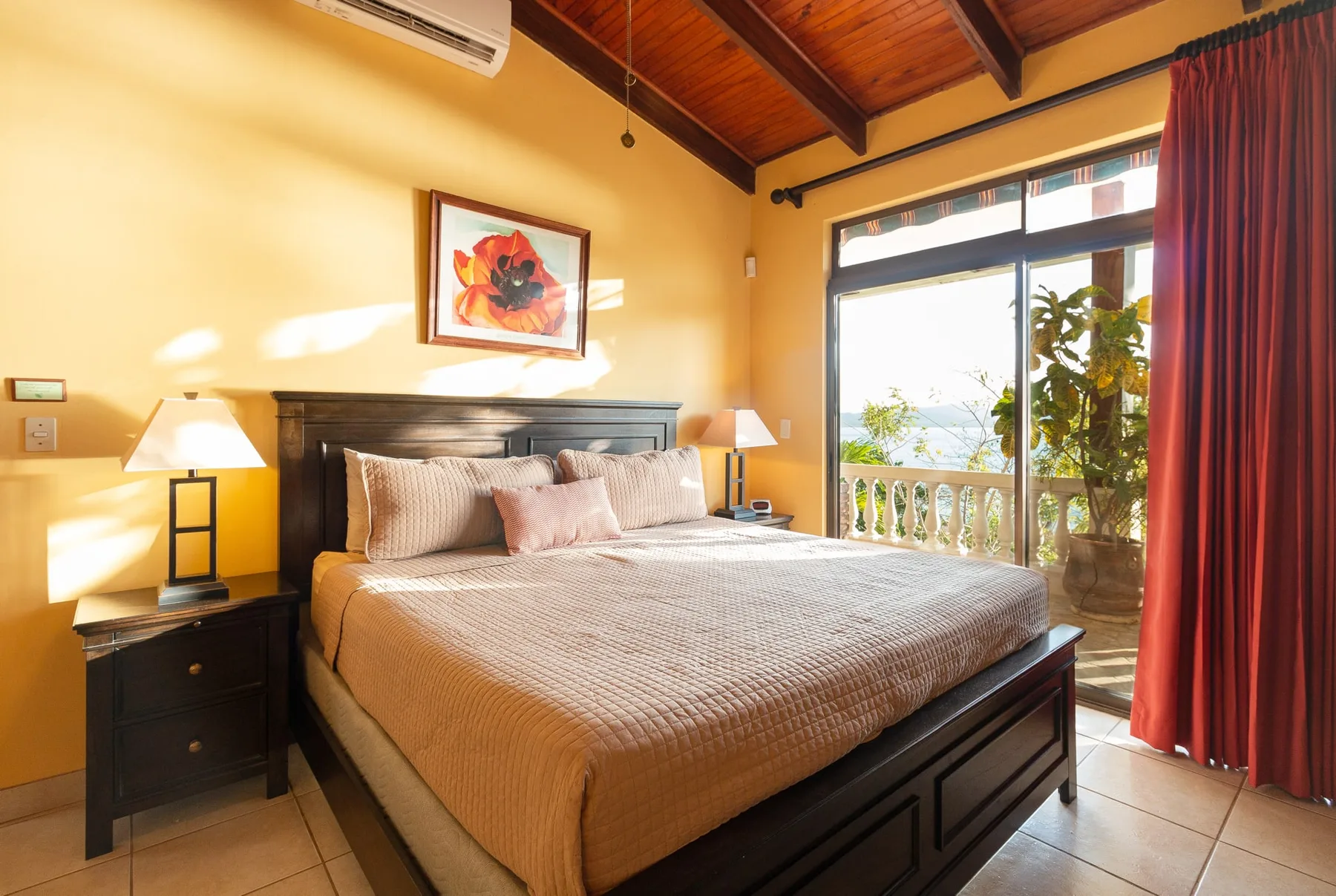 A bedroom with a large bed beside a bright window and red curtains.