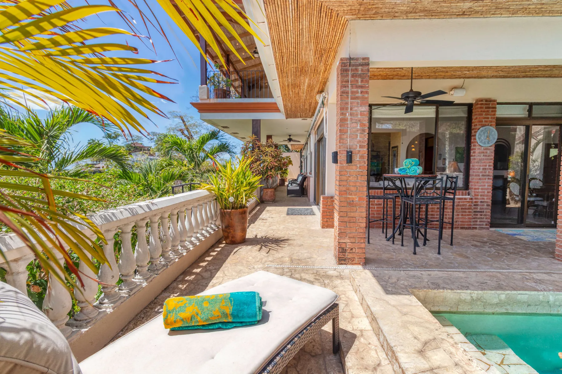 A sunny patio with outdoor seating, potted plants, and a pool.