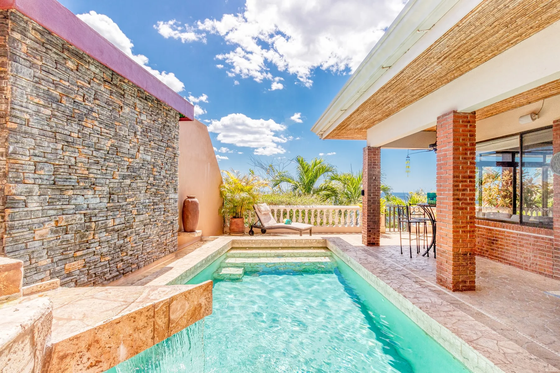 An outdoor swimming pool beside a stone wall and covered patio.