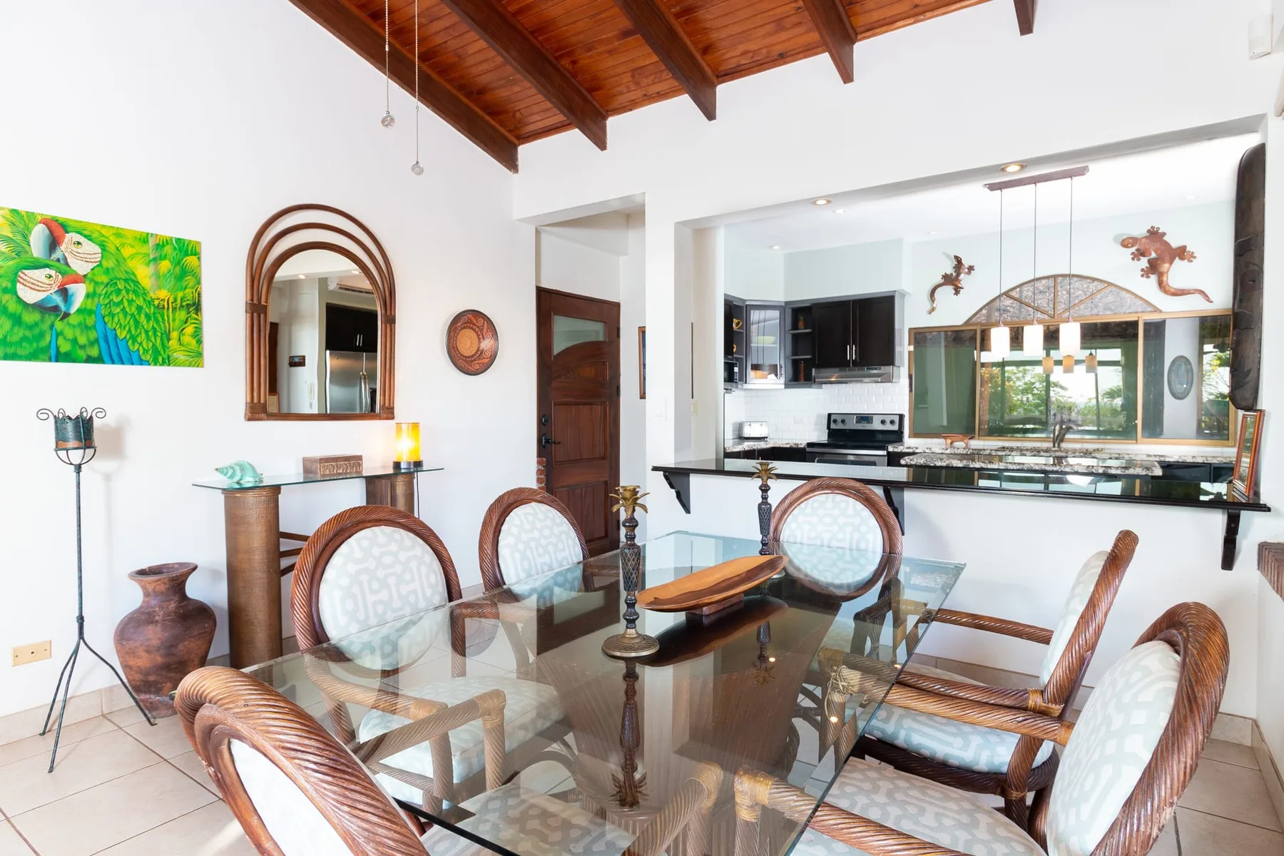 A dining area with a glass table and woven seating beneath a wooden ceiling.