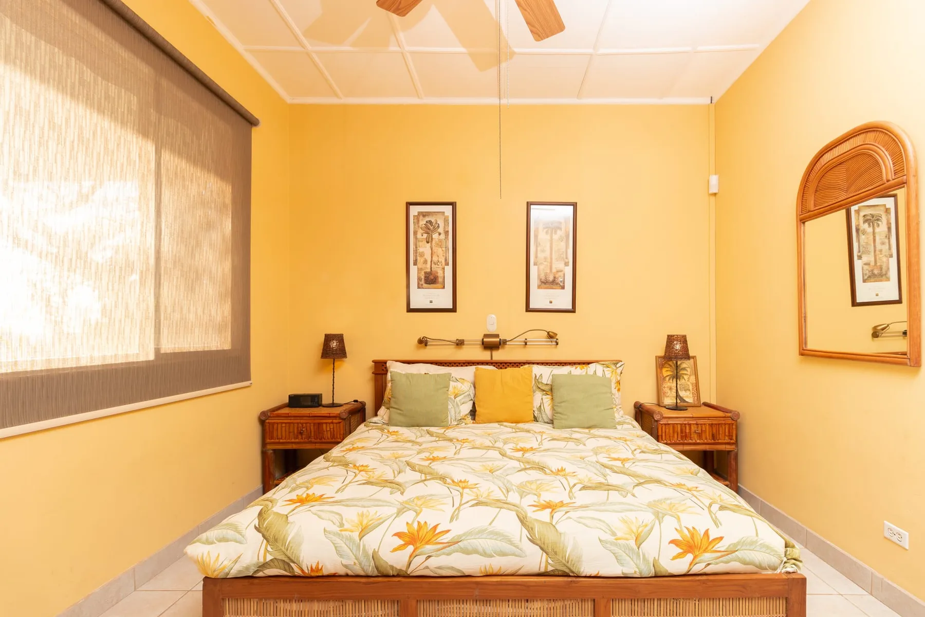 A bedroom with a bed beneath two framed pictures and matching bedside tables.