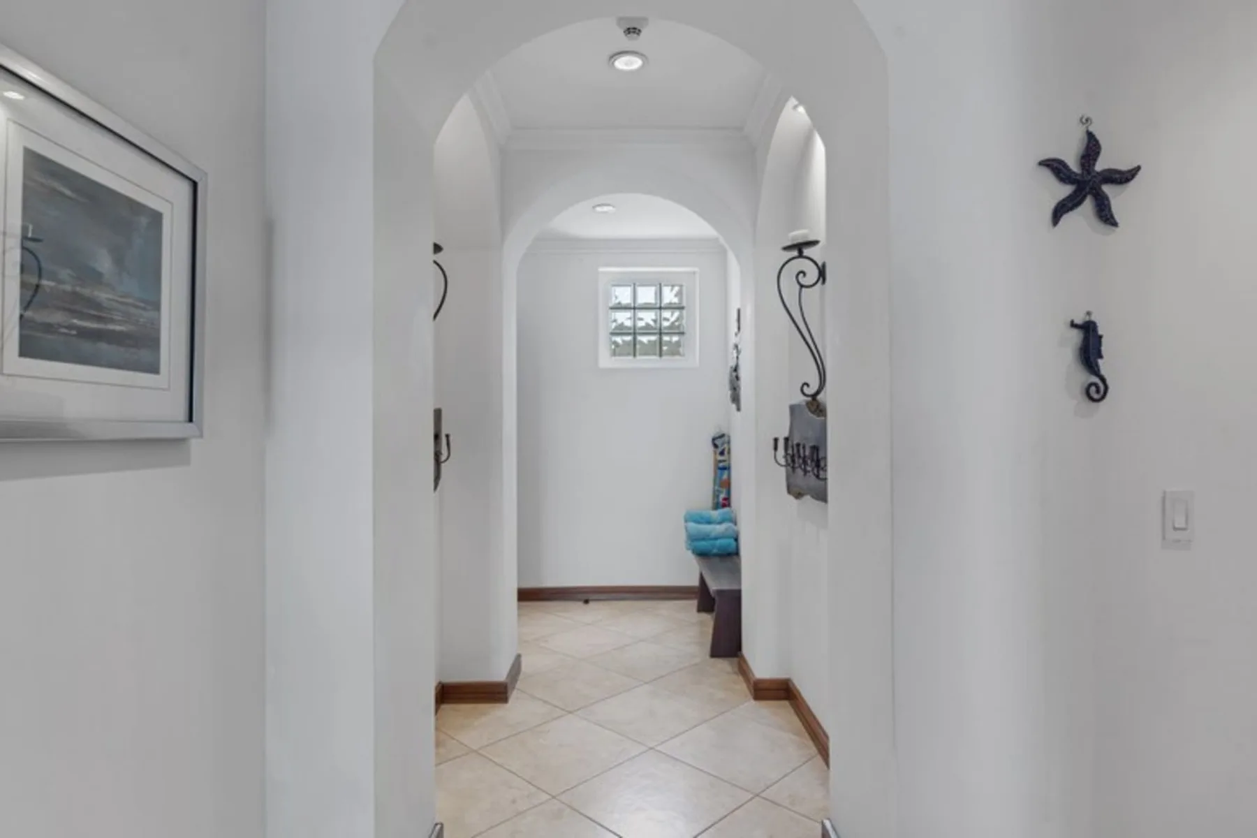 A white hallway with arched openings leads to a small window and seating.