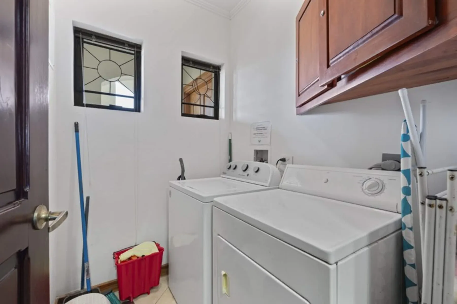 A laundry room with a washer and dryer beneath wooden cabinets.