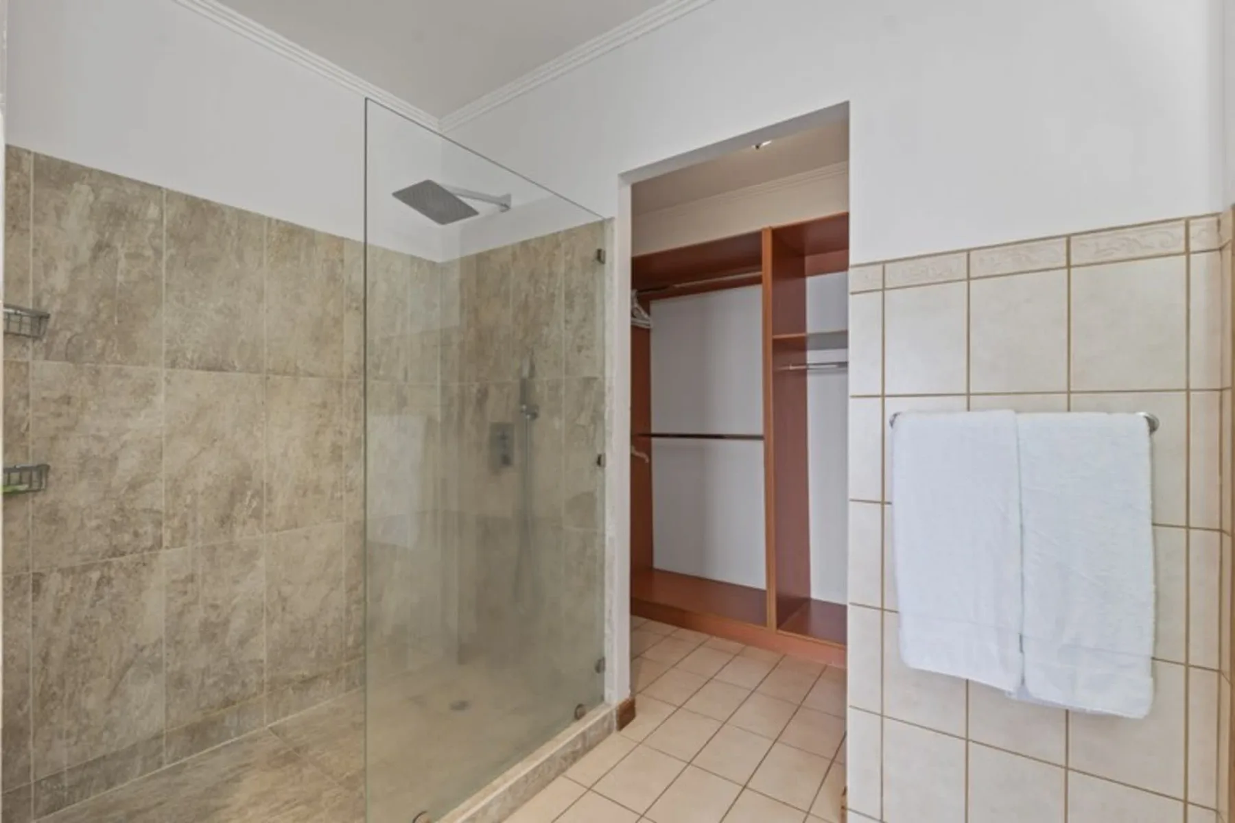 A tiled bathroom with a glass shower and an open wooden storage unit.