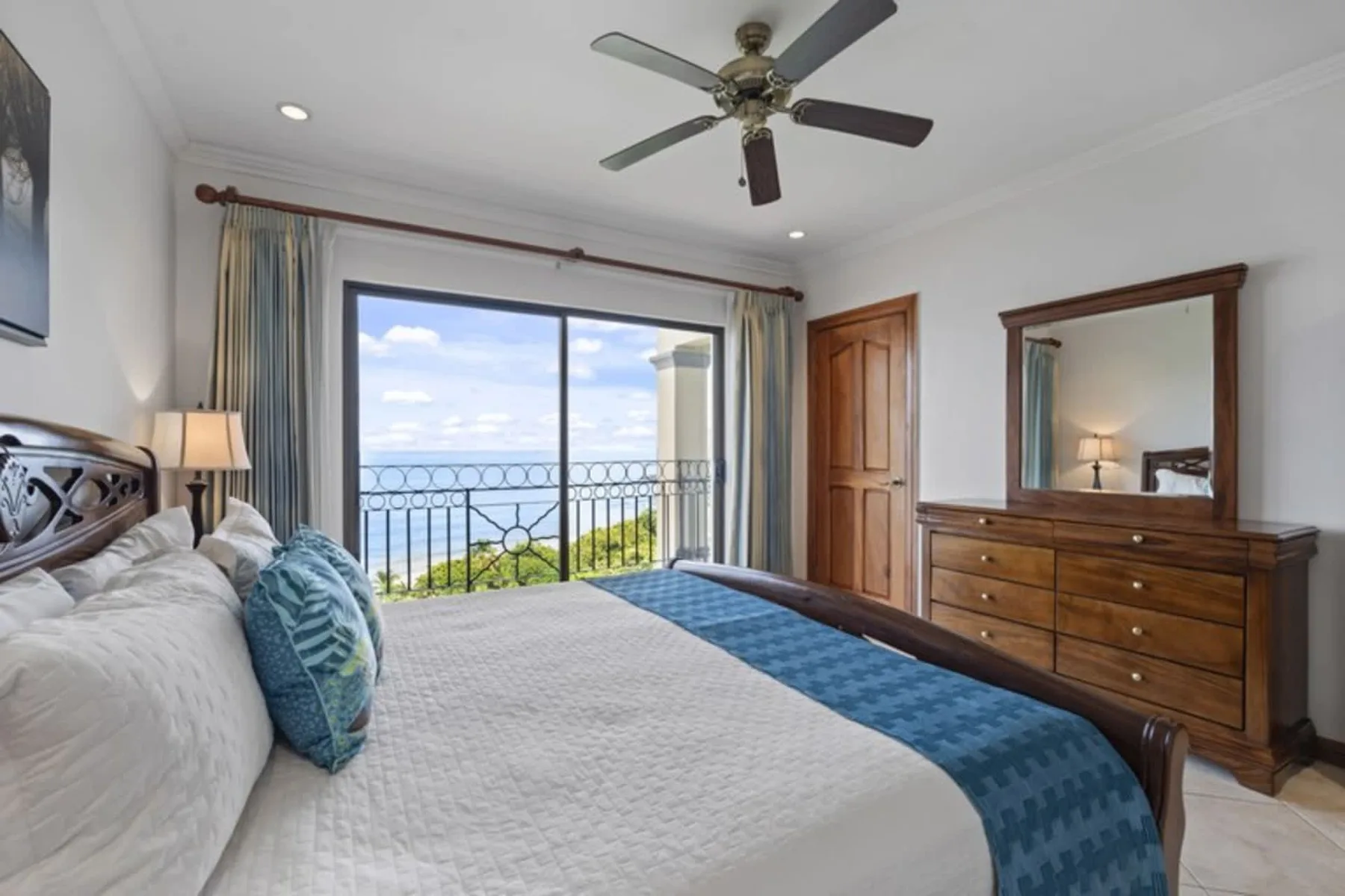 A bedroom with a bed, a dresser, and a sliding glass door opening onto a balcony.