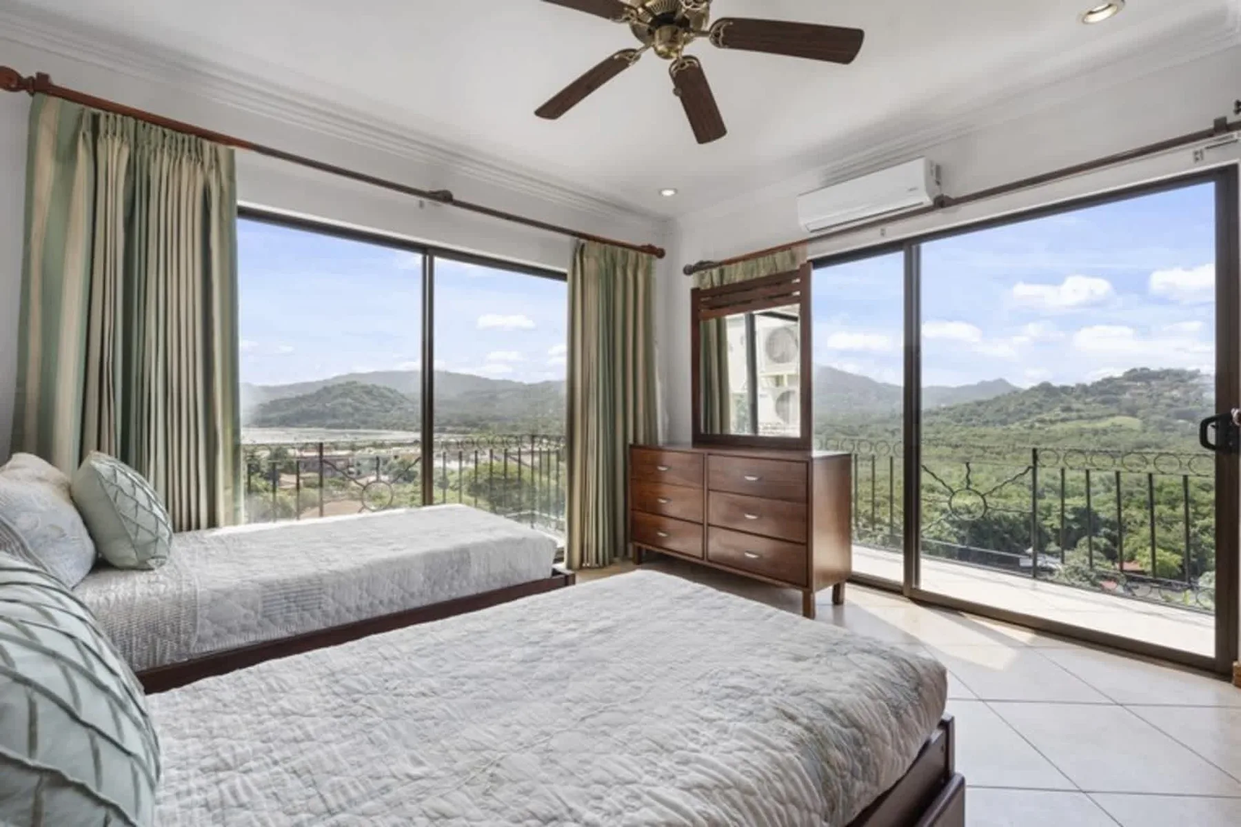 A bedroom with two beds beside large windows overlooking green hills.