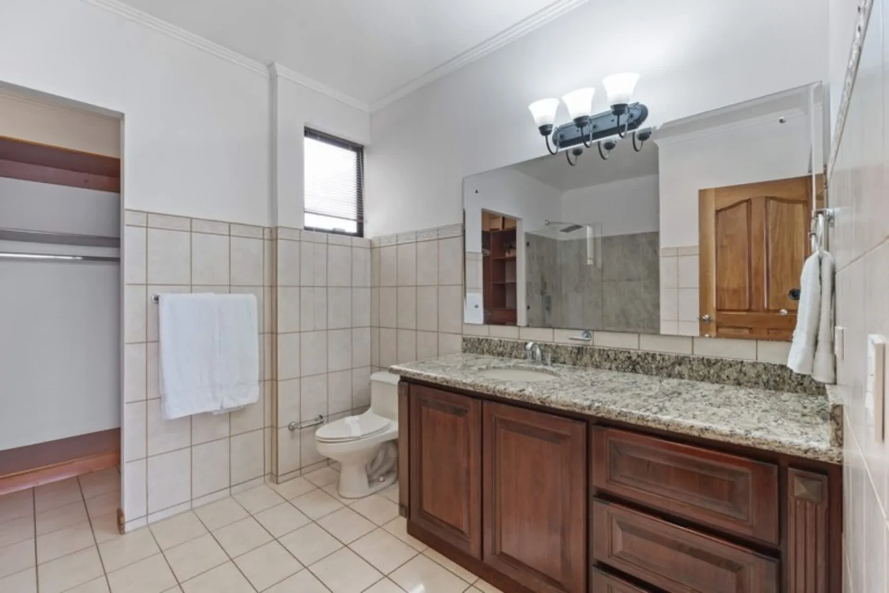 A tiled bathroom with a wooden vanity, mirror, and toilet.