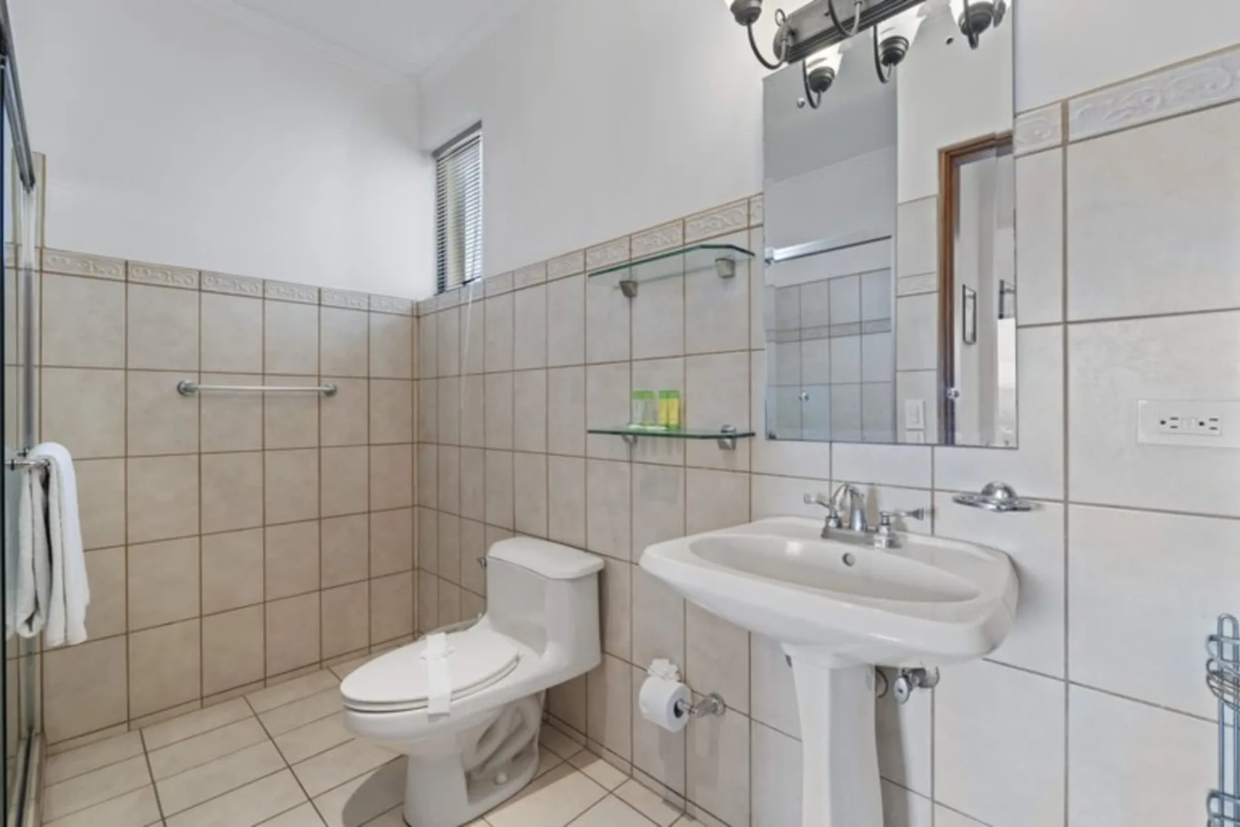 A tiled bathroom with a sink, toilet, and wall mirror.