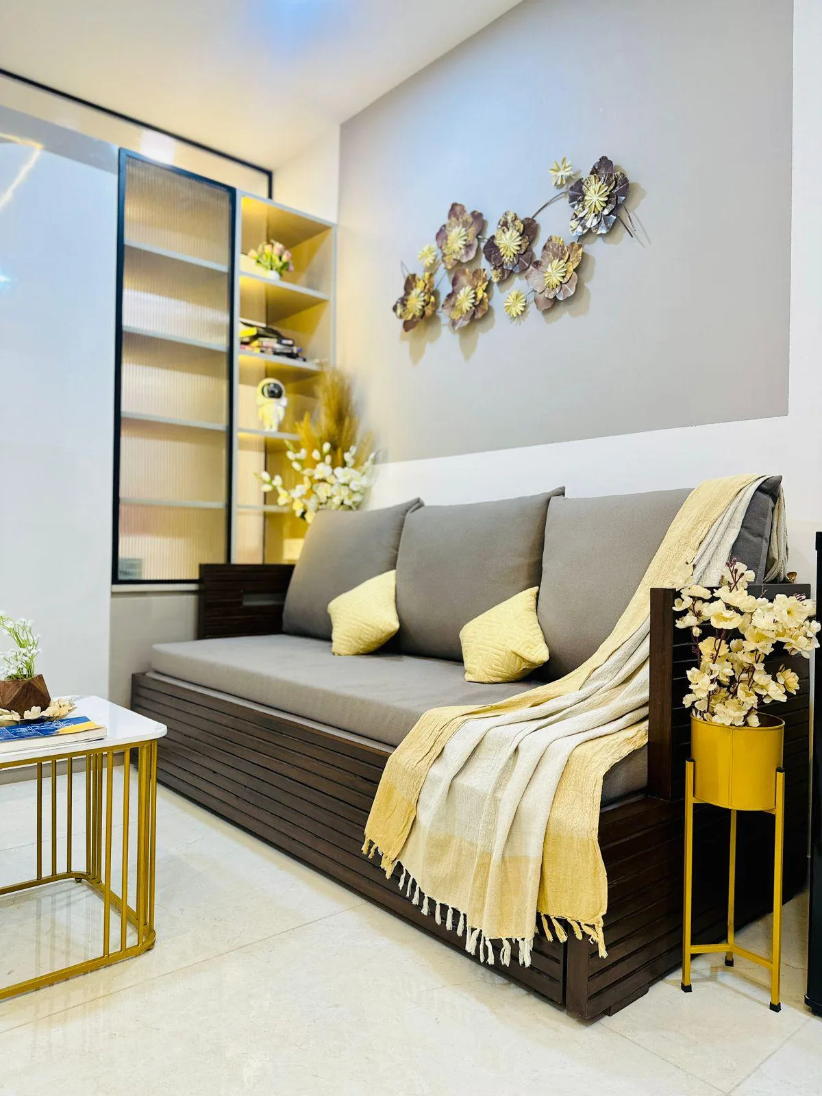 A living room seating area with a dark sofa, yellow accents, and floral wall decor.