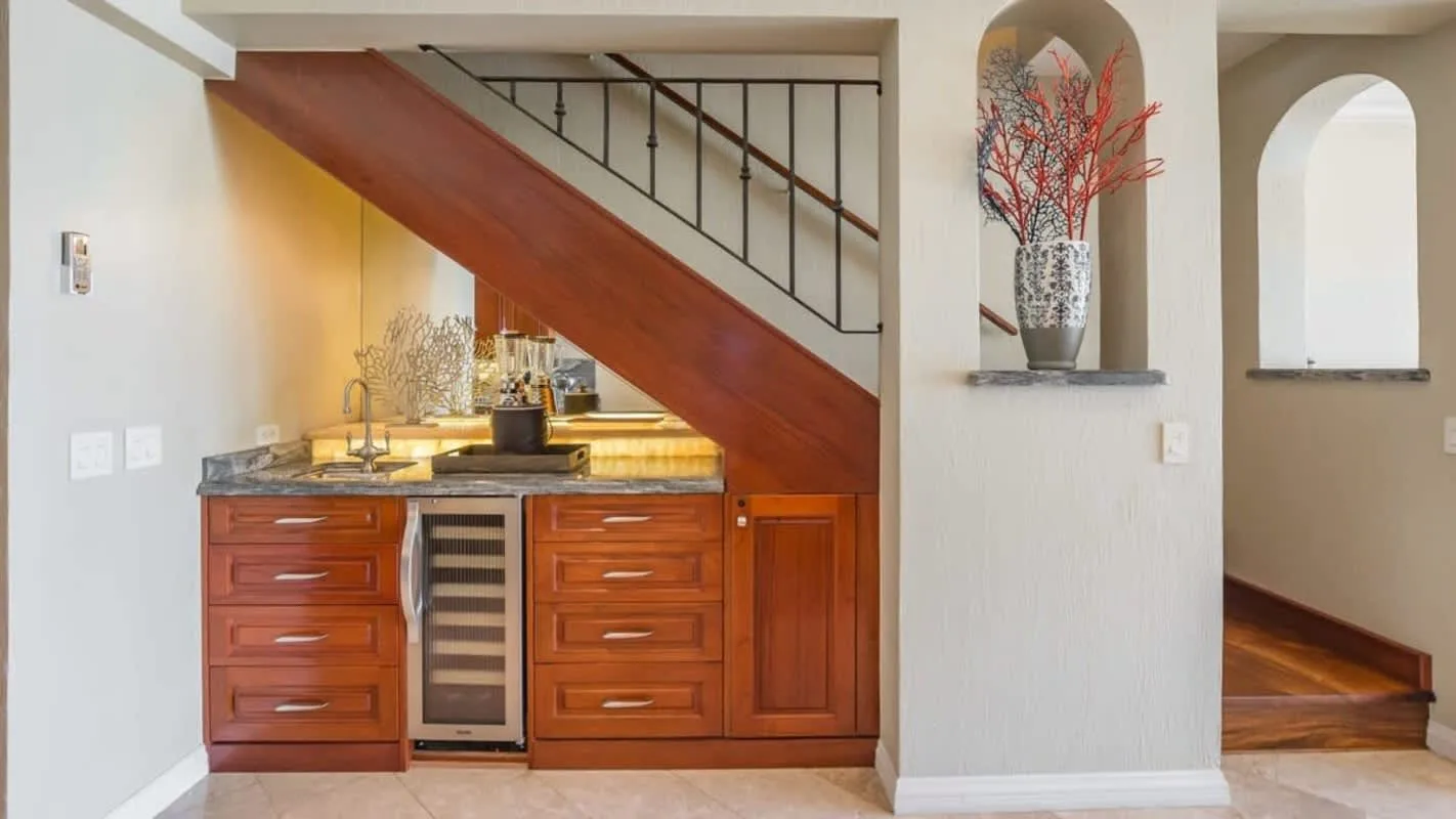 A compact kitchen sits beneath a staircase beside an arched wall niche.