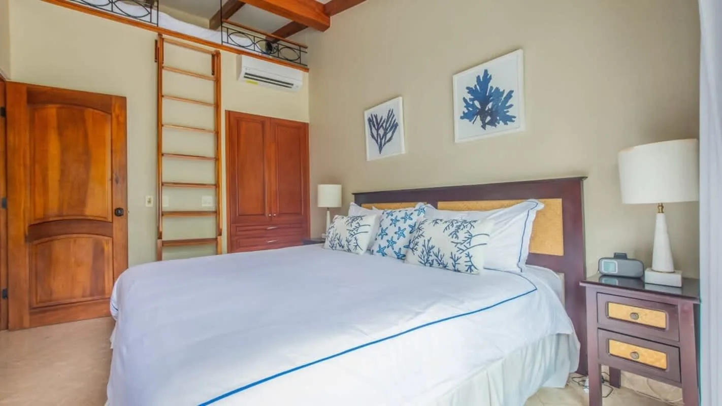 A bedroom with a large bed, blue patterned pillows, and framed botanical prints.
