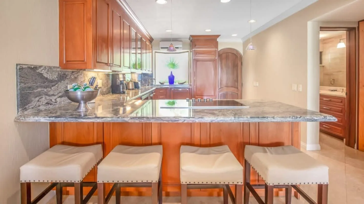 A kitchen with a broad stone island and wooden cabinetry.
