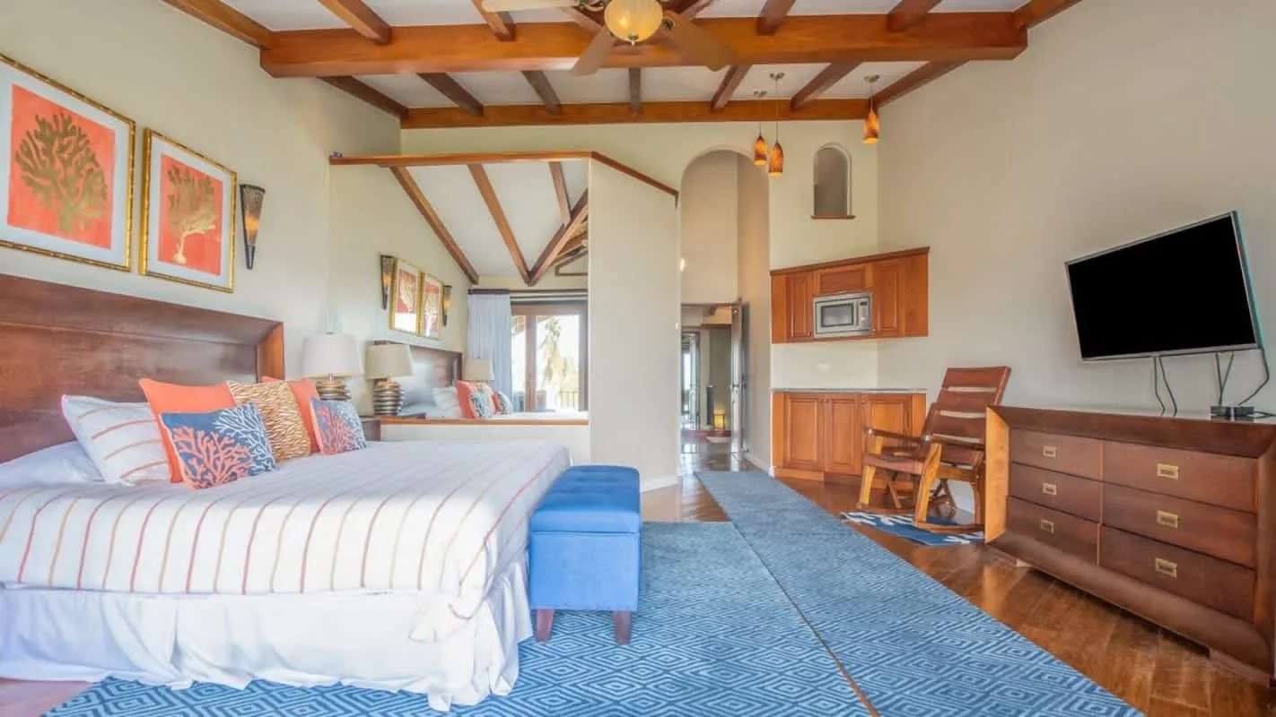 A bedroom with a large bed, blue bench, and wooden ceiling beams.