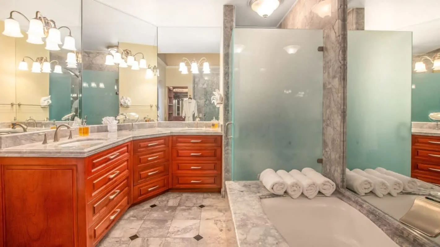 A bathroom vanity with reddish cabinets, broad mirrors, and folded towels on the counter.