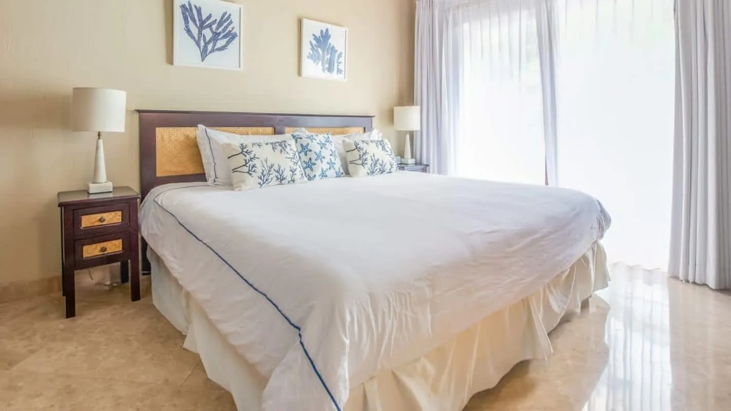 A bedroom with a neatly made bed and curtains covering a bright window.