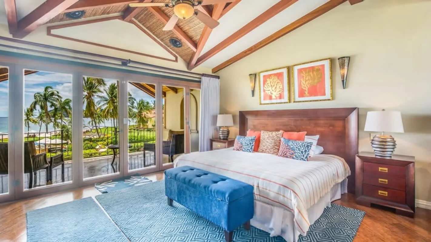 A bedroom with a large bed, blue bench, and glass doors opening onto a balcony.