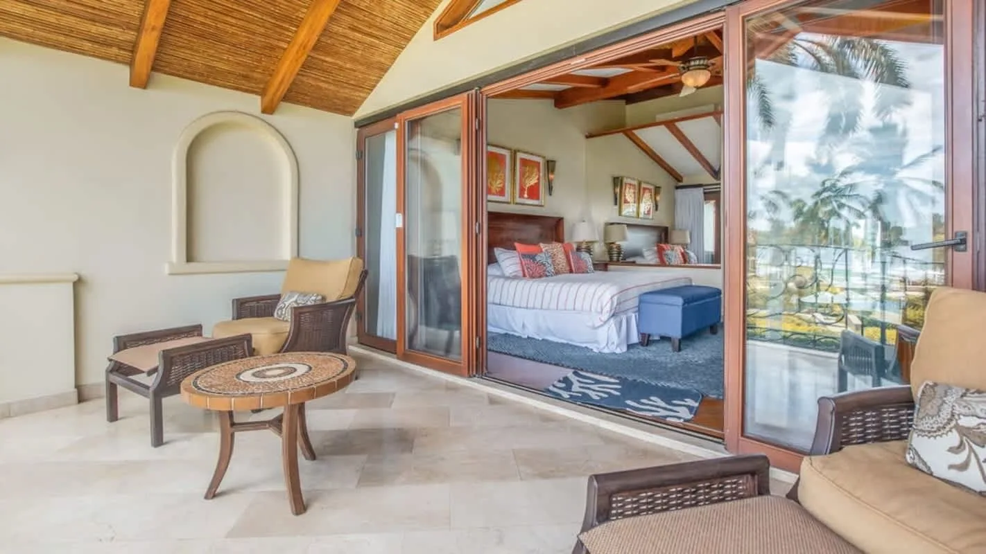 A bedroom opens onto a tiled patio with wicker seating and a small table.