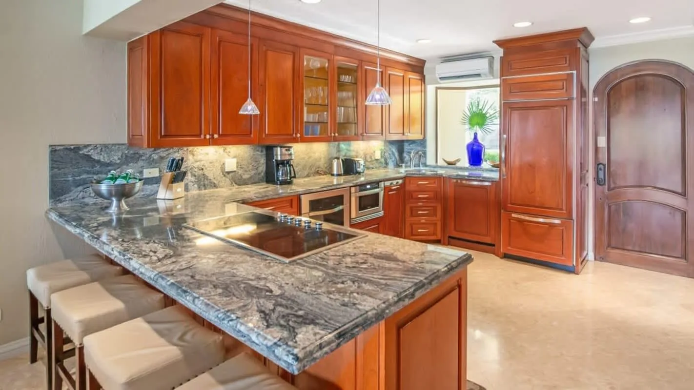 A kitchen with reddish wood cabinets, stone counters, and bar seating.