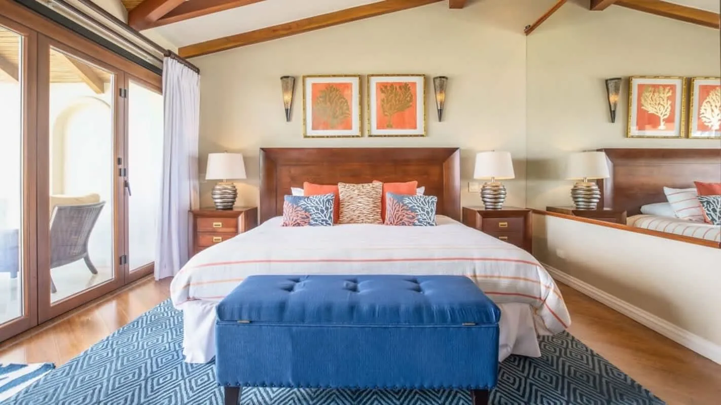 A bedroom with a large bed, blue bench, and sliding glass doors.