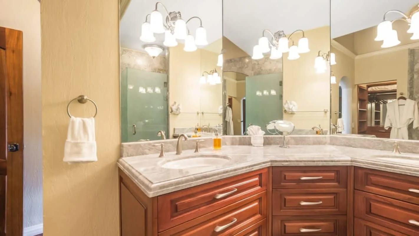 A bathroom vanity with a wide countertop, sinks, mirrors, and bright lights.