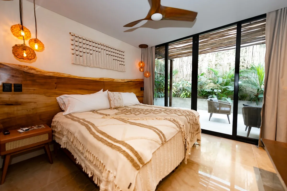 Un dormitorio con una cama junto a grandes puertas de vidrio que dan a un patio frondoso.