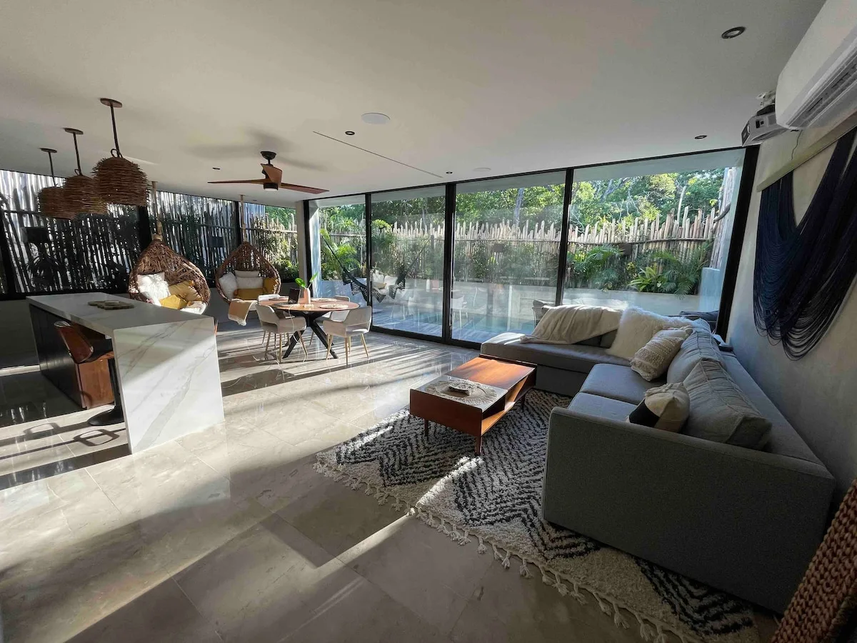 Una sala luminosa con una zona de asientos junto a grandes ventanales que dan a una piscina.