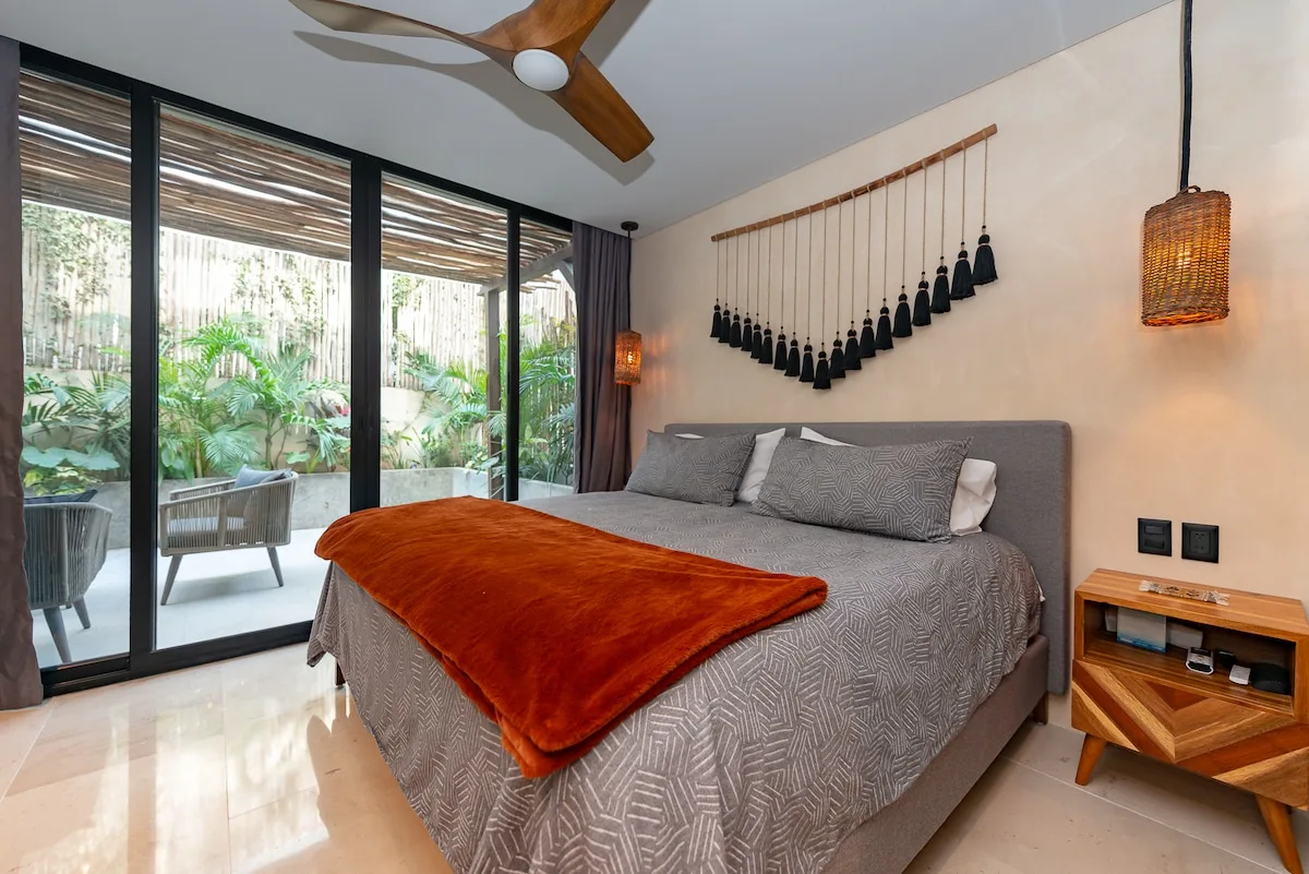 Un dormitorio con una cama junto a grandes puertas corredizas de vidrio que dan a un patio con plantas.