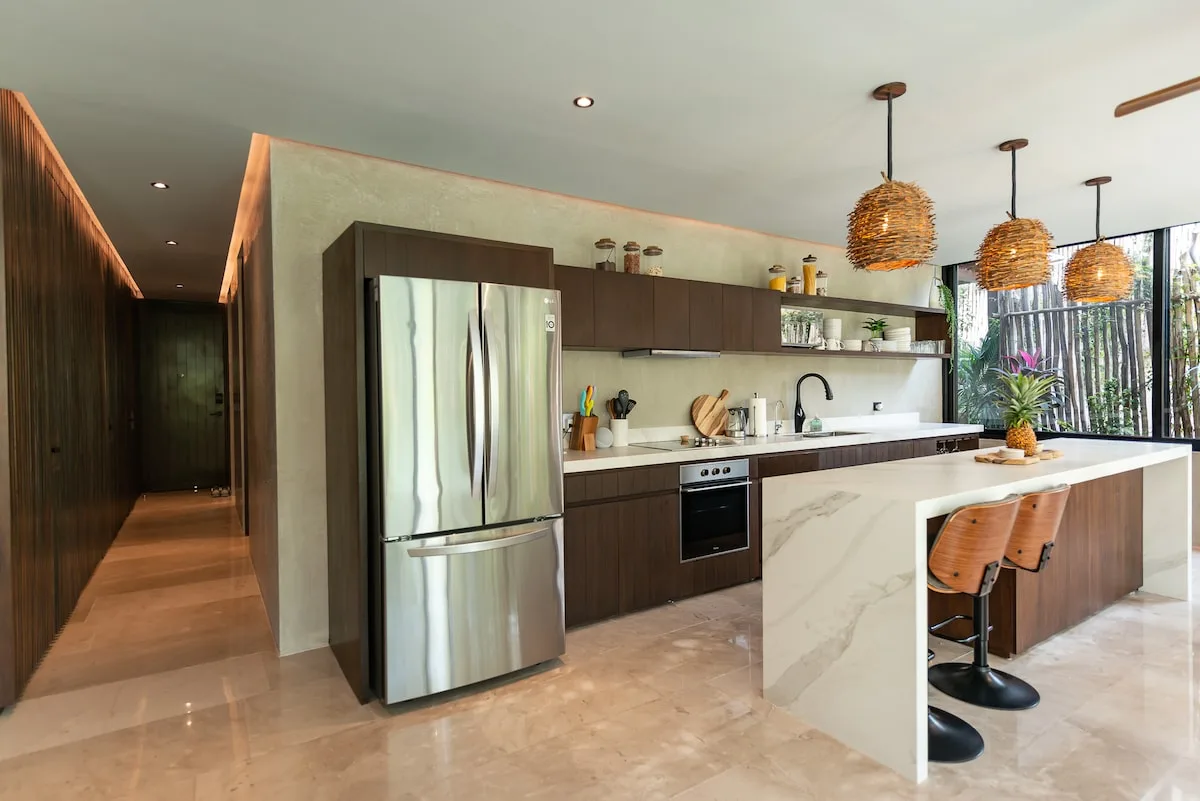 Una cocina moderna con gabinetes oscuros, electrodomésticos de acero inoxidable y una isla blanca.