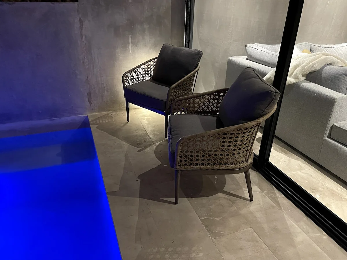 Dos sillas acolchadas están junto a una piscina iluminada de azul en una sala moderna.