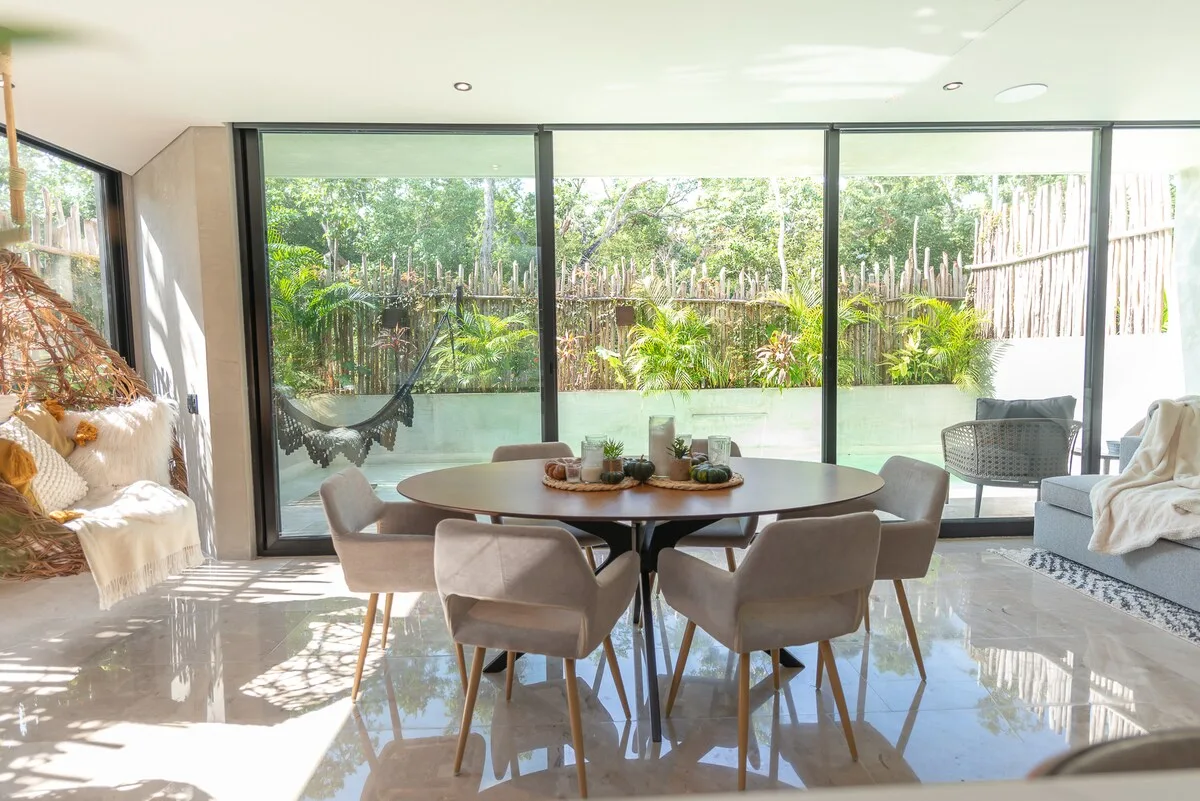 Un comedor luminoso con una mesa y asientos junto a grandes ventanales.