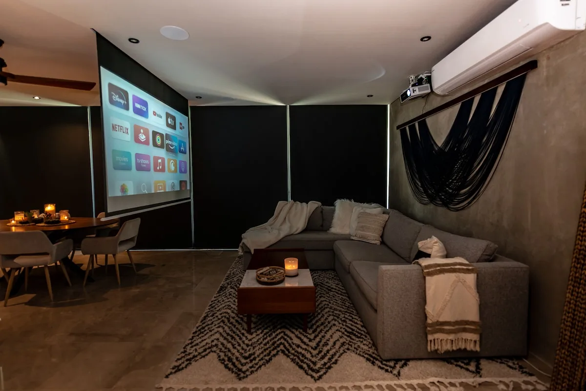 Una sala de estar con asientos seccionales y una pantalla proyectada.