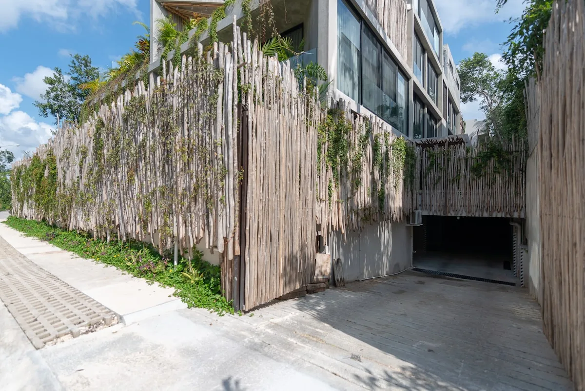 Zona común: Entrada de un edificio moderno con acceso pavimentado y una cerca vertical alta.