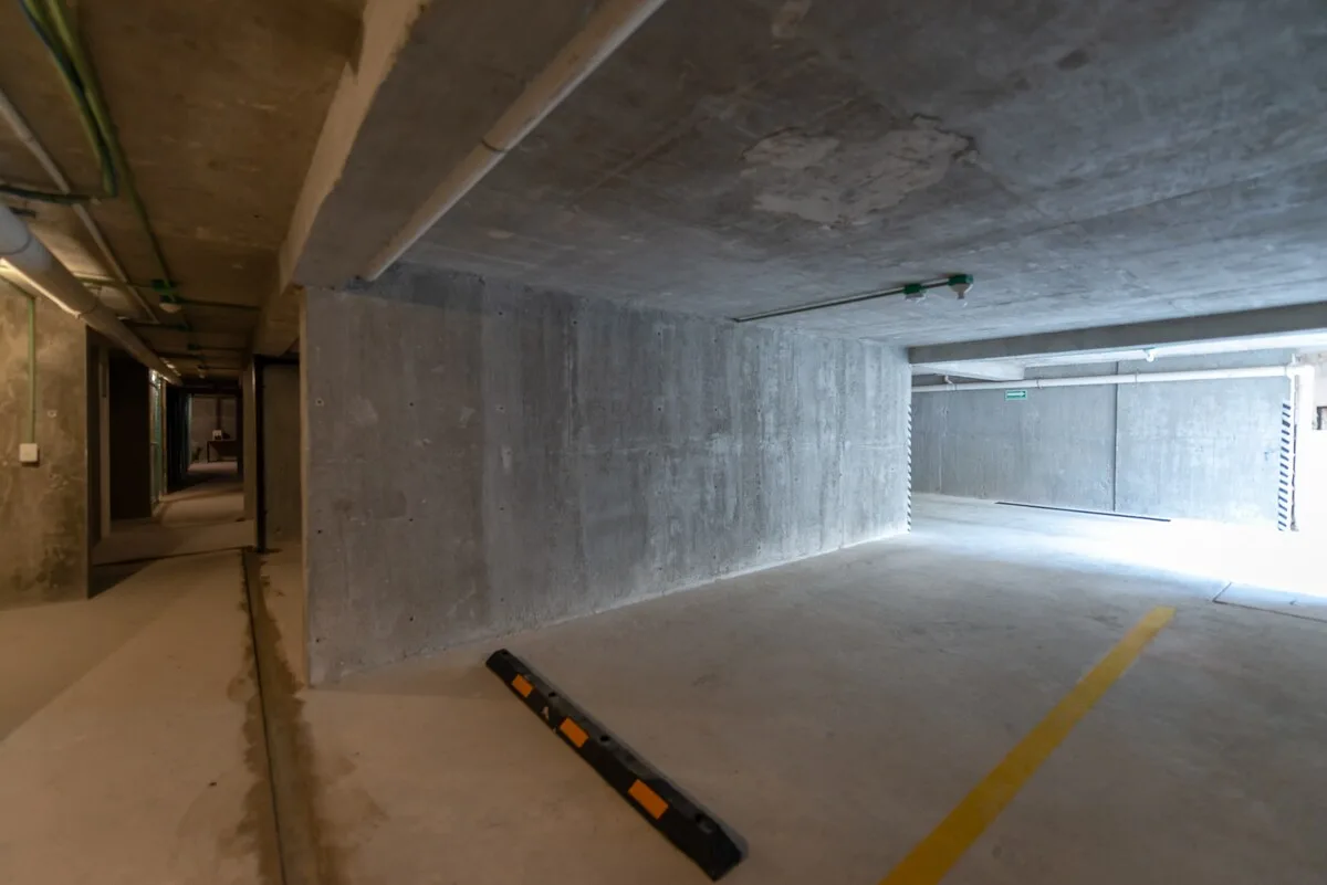 Zona común: Un estacionamiento subterráneo con paredes de concreto y marcas amarillas en el suelo.