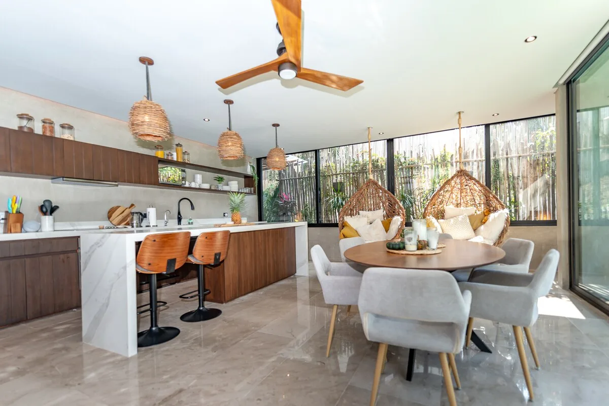 Una cocina abierta con comedor, mesa y lámparas colgantes tejidas.