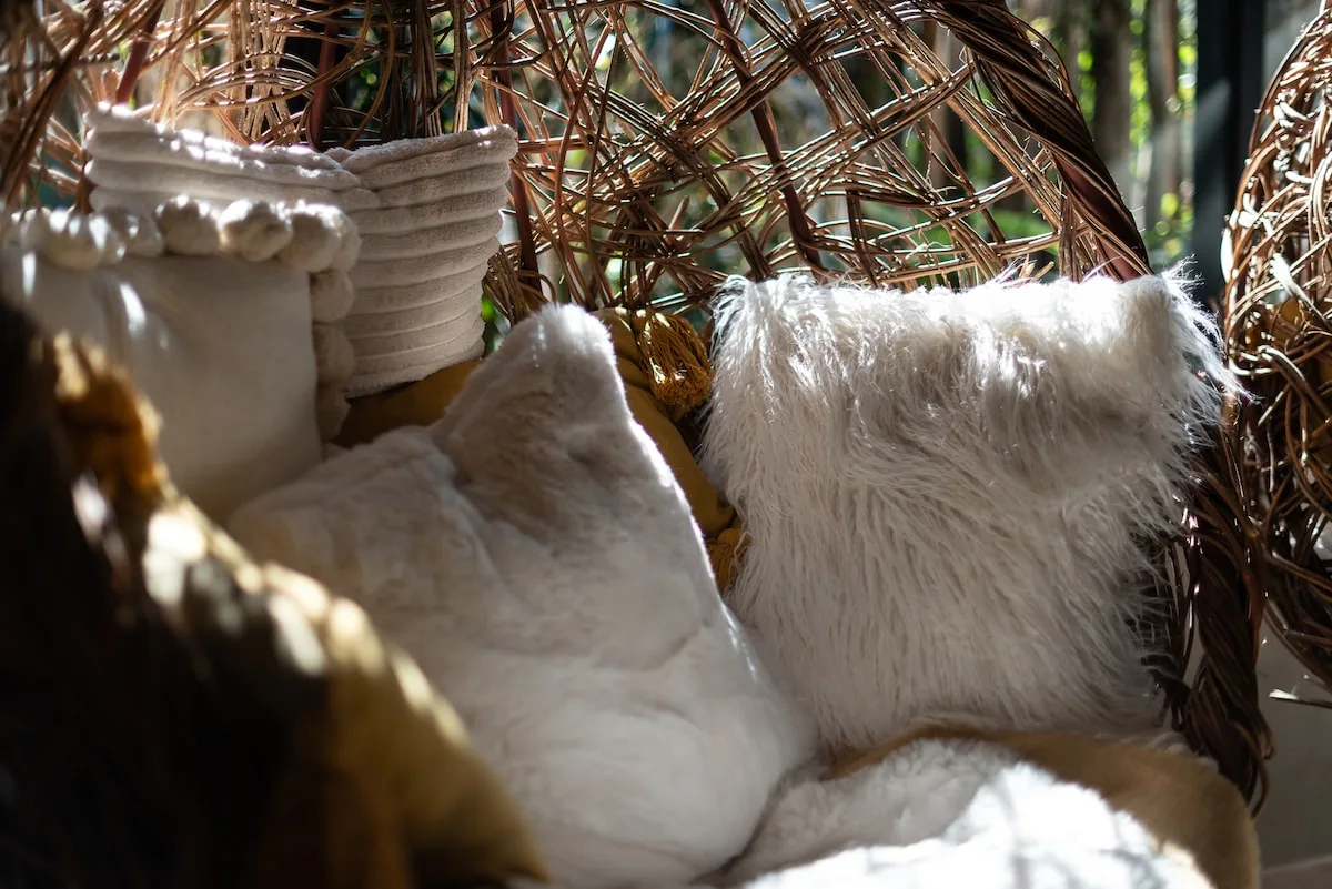 Un rincón acogedor con cojines blancos y muebles de mimbre.