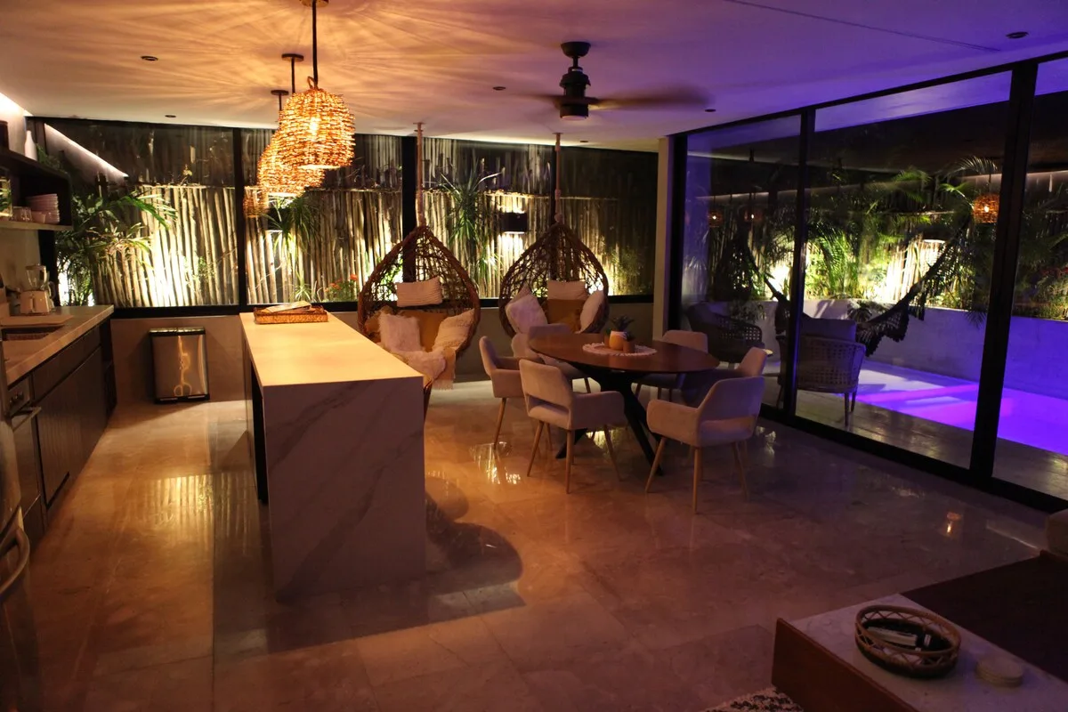Comedor con iluminación cálida y una mesa junto a grandes ventanales.