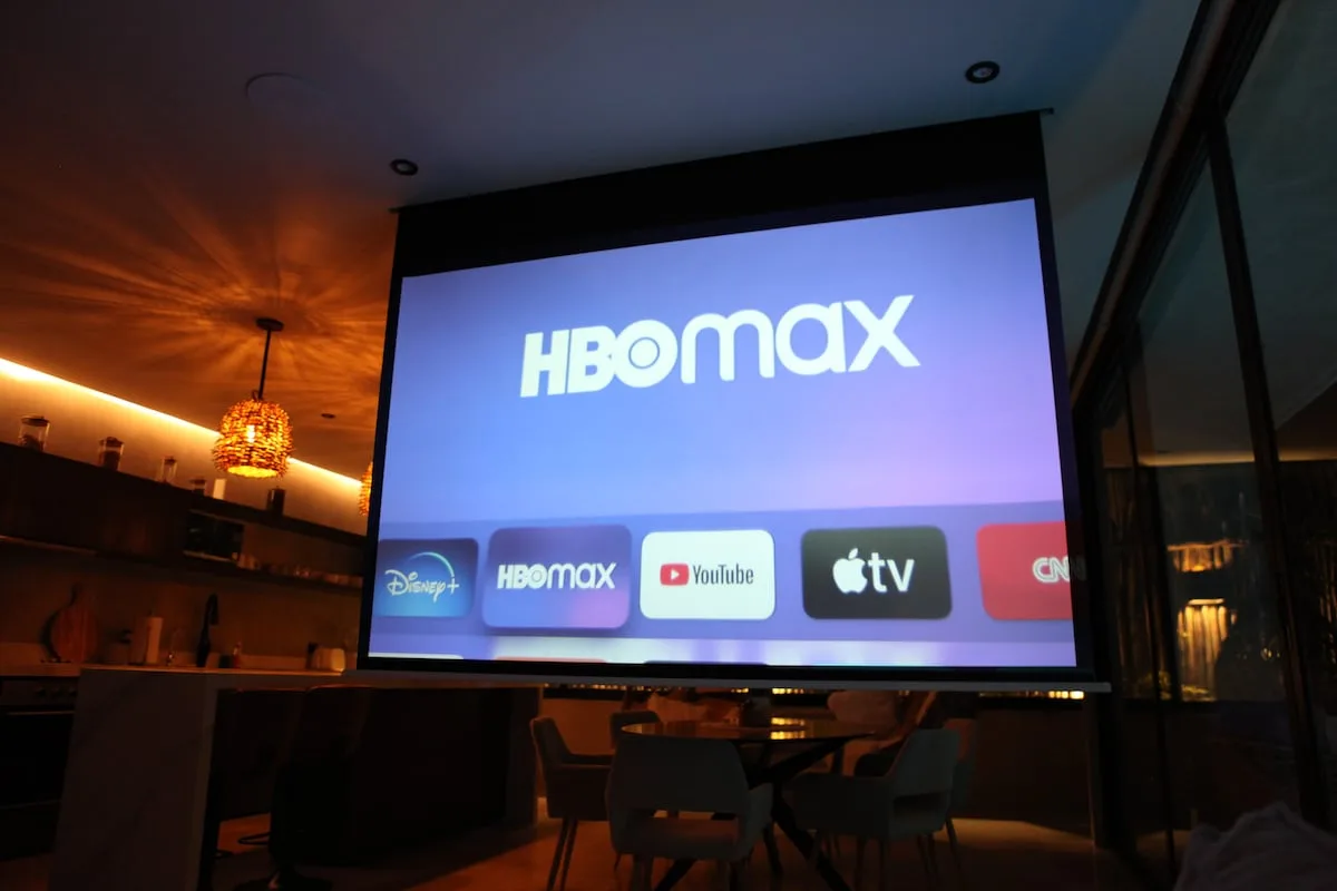 Una pantalla grande muestra logotipos de servicios de streaming en un comedor con poca luz.