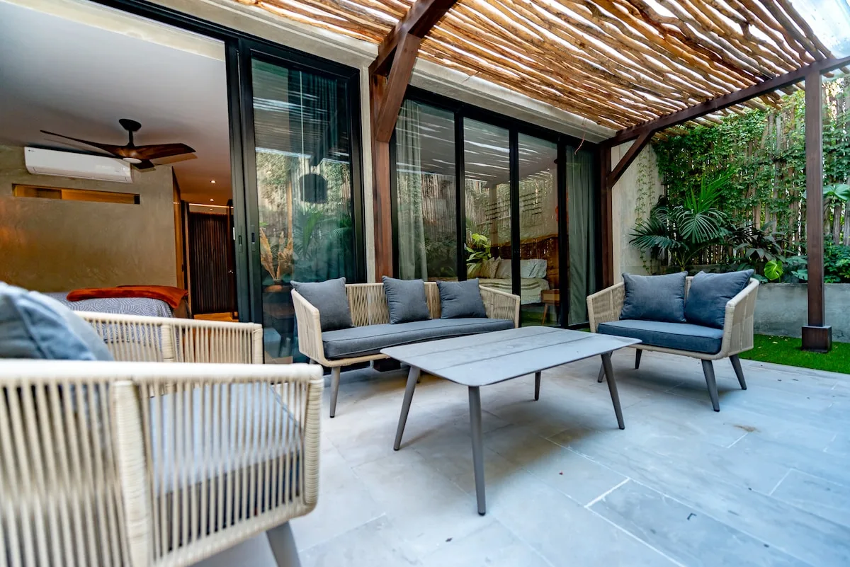 Un patio cubierto con asientos al aire libre y una mesa baja junto a puertas de vidrio.