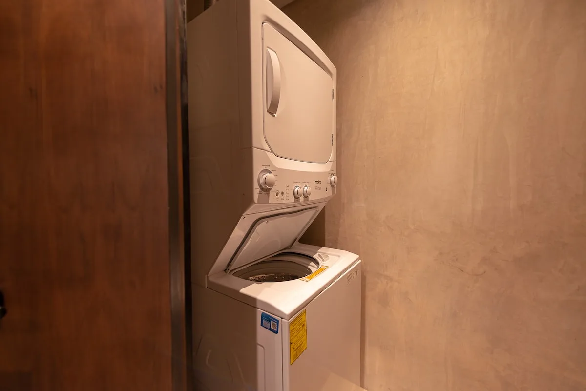 Zona de lavandería con lavadora y secadora apiladas junto a una pared beige.