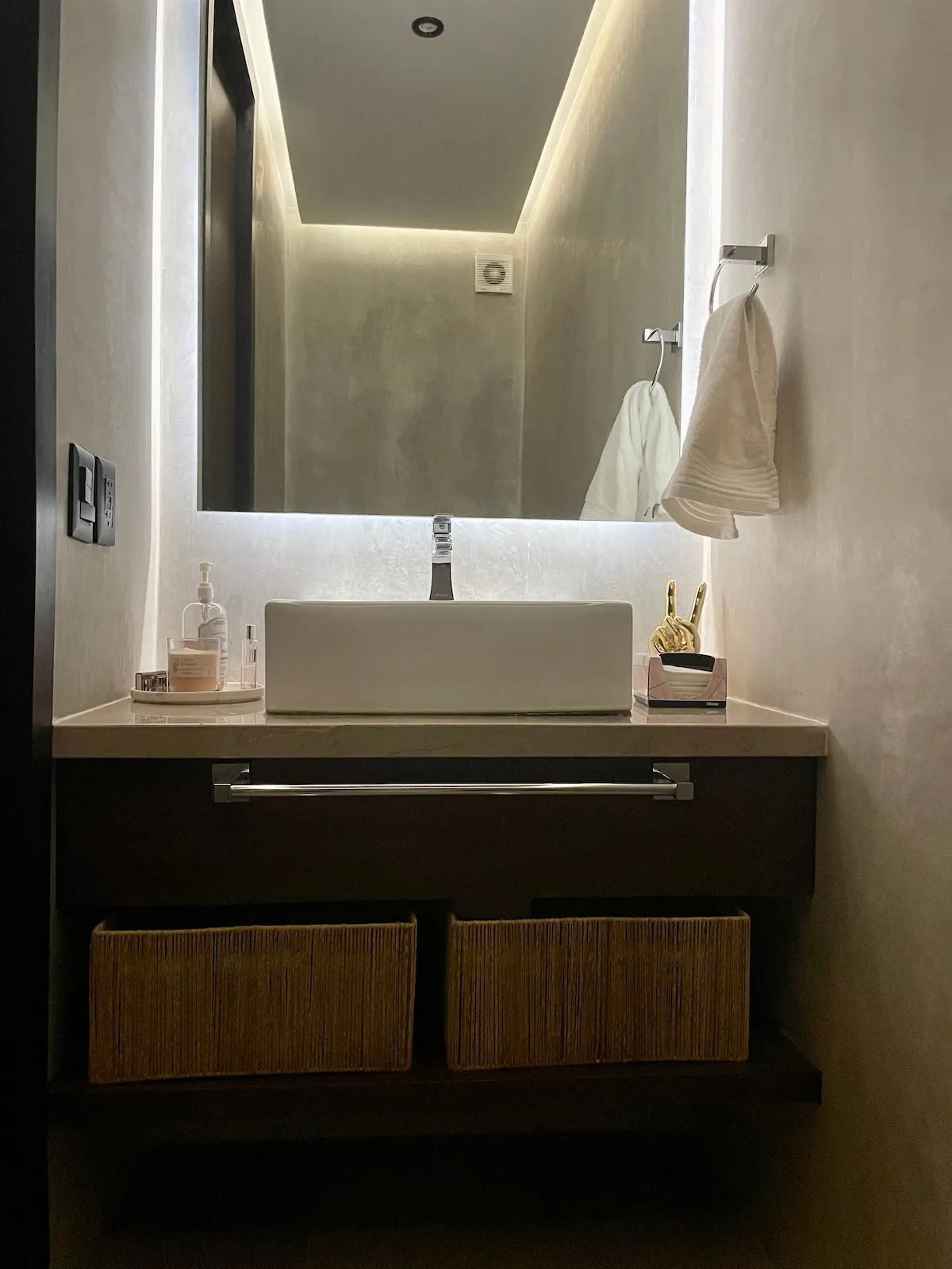Un lavabo de baño con un lavamanos rectangular, espejo de pared y toallas colgadas.