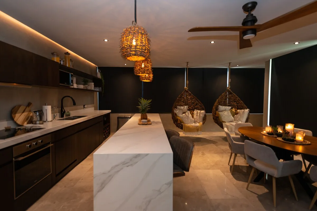 Una cocina moderna y zona de comedor con una isla blanca y sillas colgantes.