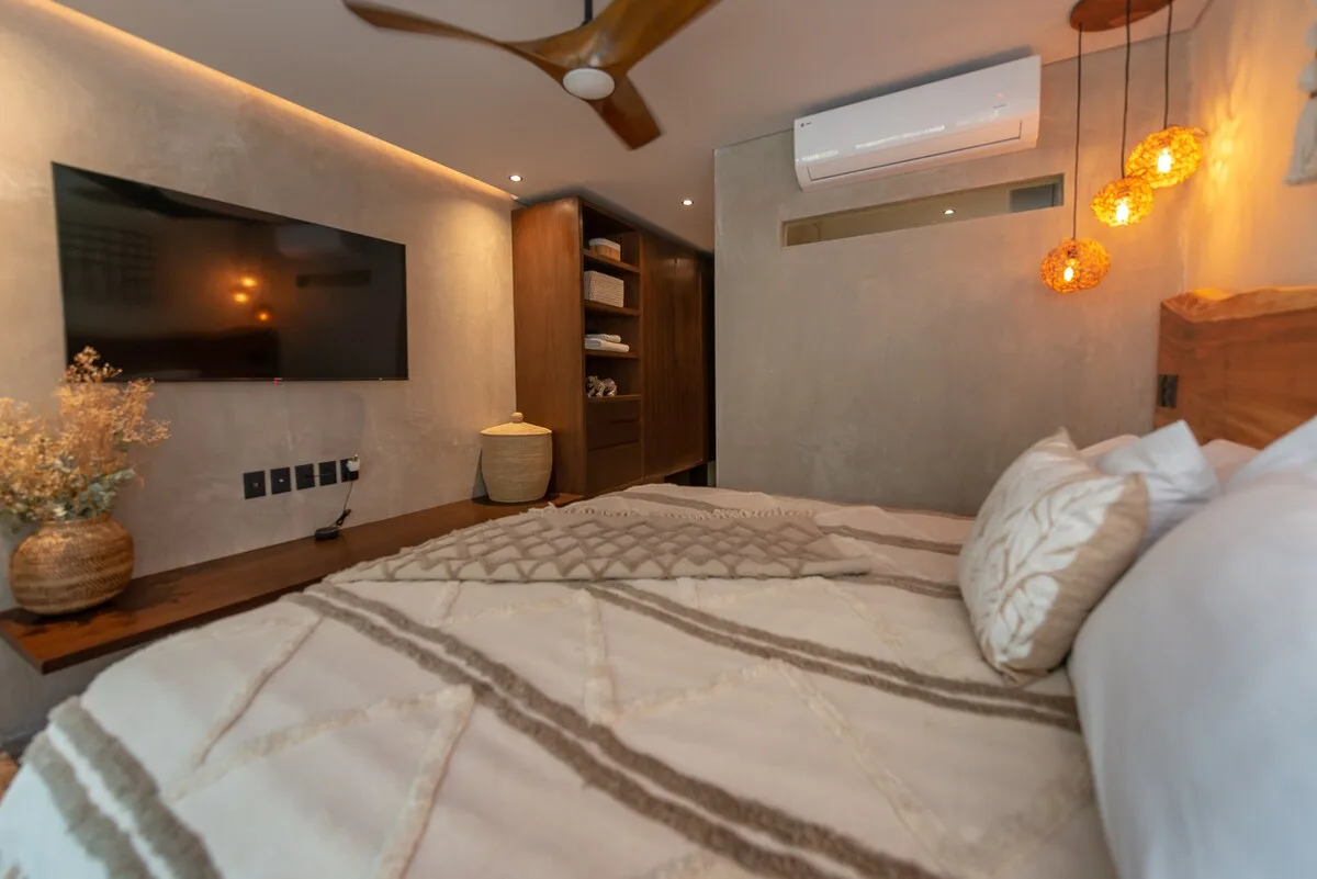 Un dormitorio con cama, televisor en la pared y luces colgantes cálidas.