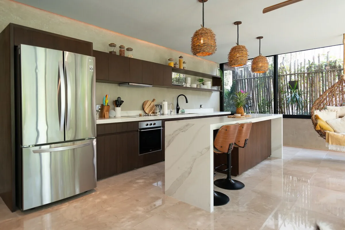 Una cocina moderna con isla de mármol, asientos de barra y grandes ventanas.