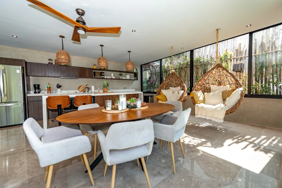 Una cocina abierta y comedor con una mesa y sillas colgantes junto a grandes ventanales.