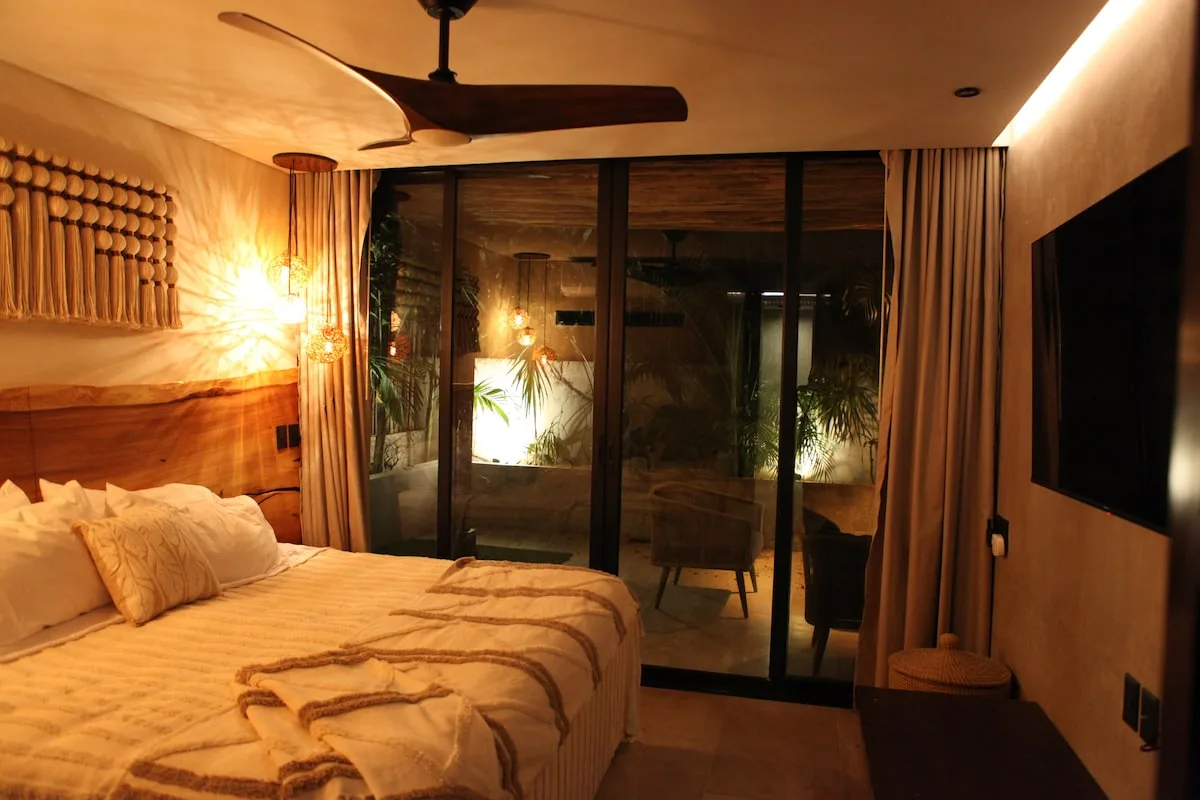 Dormitorio cálido y bien iluminado, con una cama frente a puertas de cristal y un televisor en la pared.